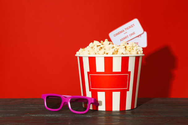 3d glasses, striped bucket with popcorn and tickets against red  - Photo, image
