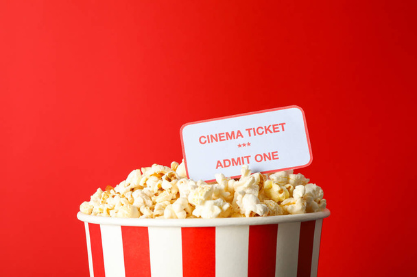 Striped bucket with popcorn and tickets against red background - Фото, изображение