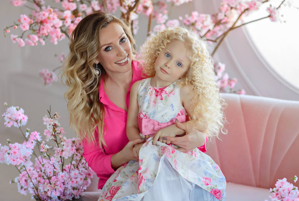Beautiful blonde mom hugs a very cute curly blonde daughter in a - Photo, image