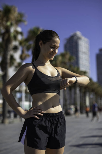 Mooie vrouw het controleren van haar activiteit armband of armband voor of na het sporten of rennen in Barcelona - Foto, afbeelding
