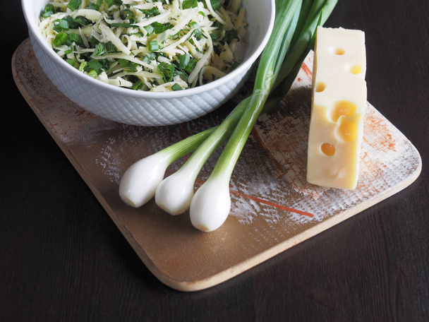 Fresh cheese with holes, green onions, herbs on the table. Useful filling of grated cheese with herbs and green onions to prepare for a delicious salad, roll, lavash, pizza, pita - Photo, Image