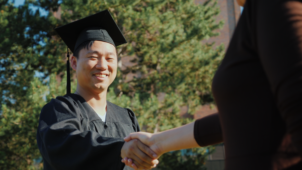Exitoso hombre asiático en ropa de graduado acepta felicitaciones. Le dan la mano.
 - Imágenes, Vídeo