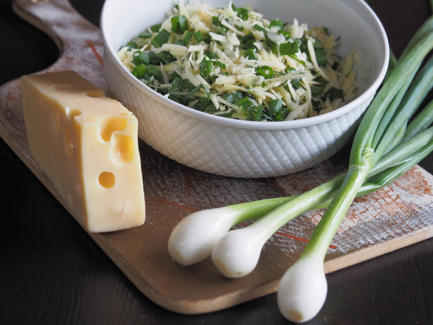 Fresh cheese with holes, green onions, herbs on the table. Useful filling of grated cheese with herbs and green onions to prepare for a delicious salad, roll, lavash, pizza, pita - Photo, Image