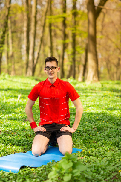 Man spreads a blue yoga mat in a park on green grass for exercises and relaxation. Healthy lifestyle - Photo, Image