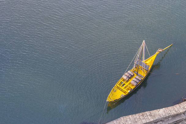 Yellow boat with wine barrels view from above. Boat on water top aerial view. Yellow wooden boat in Porto, Portugal. Vintage kayak on river Douro, Portugal. Water transport concept.  - Photo, Image