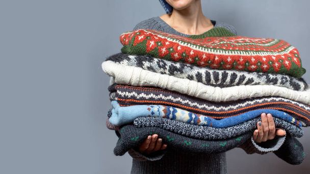 Young woman hold pile of sweaters wearing knitted hat and warm wool sweater - Foto, Bild