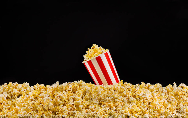 Paper striped bucket installed on scattered popcorn isolated on black background - Foto, imagen