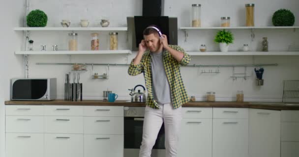 Young attractive man is dancing and listening music in his kitchen - Video