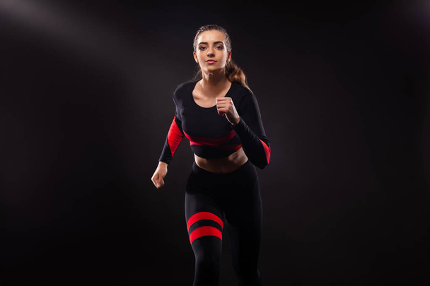 Strong athletic woman sprinter, running on black background wearing in the sportswear. Fitness and sport motivation. Runner concept with copy space. - Foto, Imagen