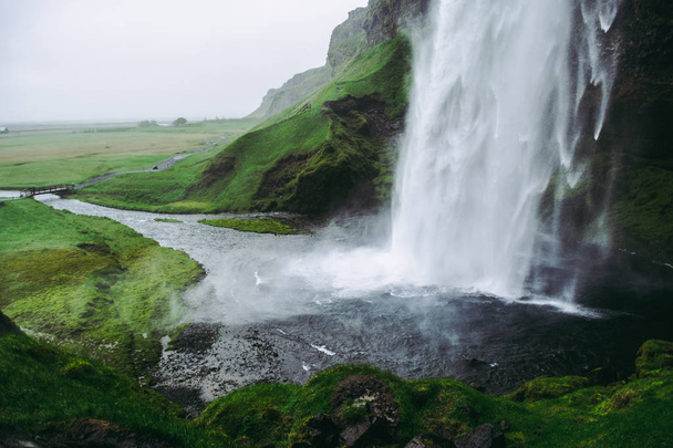 Cold pale white water of Seljalandsfoss  waterfall in Iceland. Typical windy weather. - Photo, Image