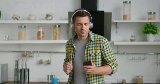 Young cheerful man is listening music and dancing, wearing wireless headset - Séquence, vidéo
