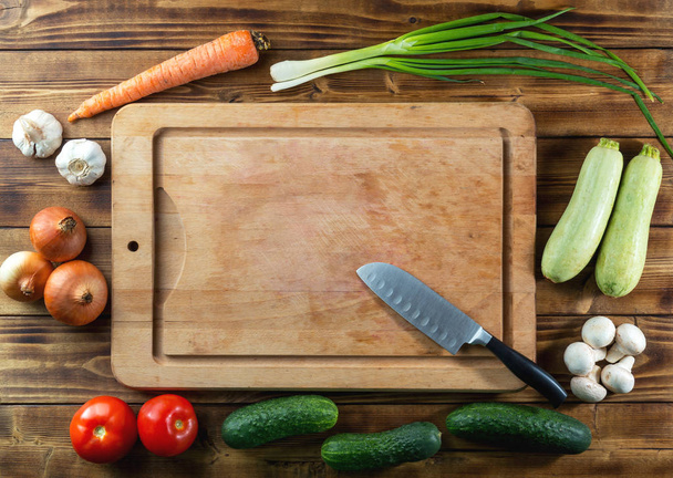 Used rustic wooden chopping board, knife and raw vegetables on dark background, top view, copy space - Photo, Image