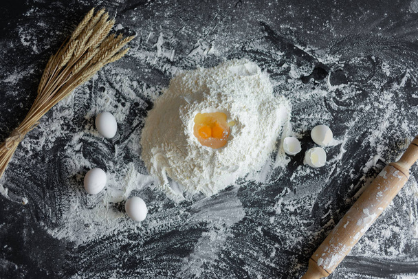 Ingredients for baking - dough, flour, wooden spoon, rolling pin, eggs, egg yolks on a dark background. - Foto, afbeelding