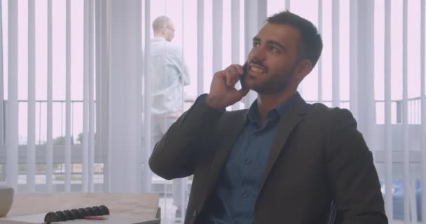 Closeup portrait of attractive businessman having a phone call talking cheerfully in the office indoors on the workplace - Кадри, відео