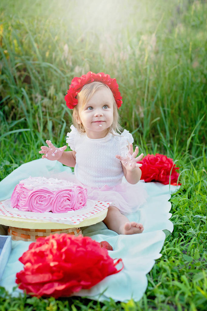 Two years old girl sitting near celebration decorations and birthday cake in green grass  - Fotoğraf, Görsel
