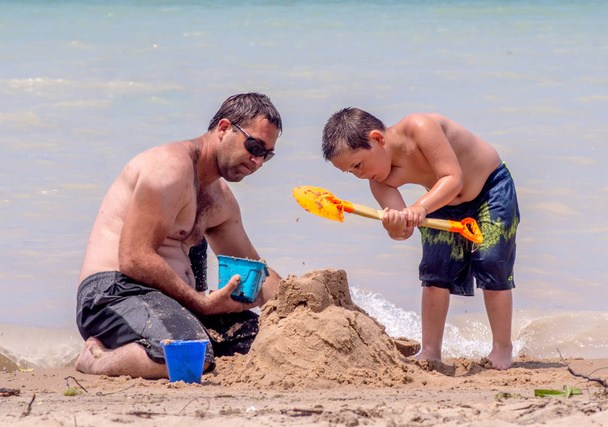 お父さんと息子はビーチで城を建てる - 写真・画像