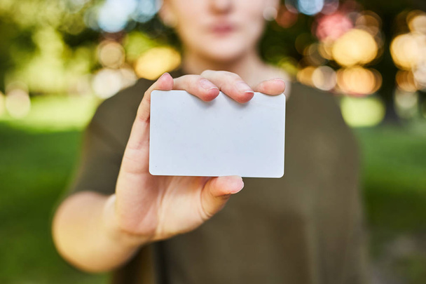 Κορίτσι κρατώντας μια λευκή πιστωτική κάρτα στα χέρια της για ψώνια.  - Φωτογραφία, εικόνα