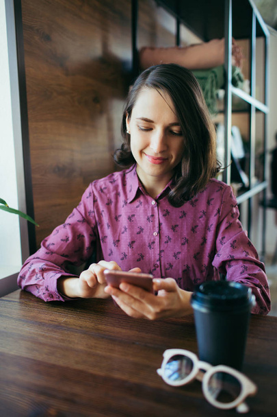 Young woman scrolls her smartphone, sitting in a cafe. - Zdjęcie, obraz