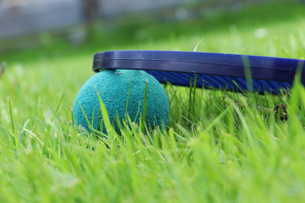 A look at the past, the times when we were children. Detail on softenis ball and racket. Best game in childhood. Toys forgotten in the grass - Photo, Image