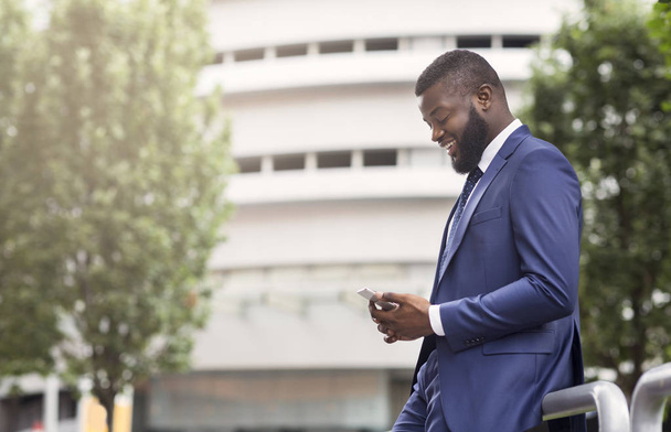 Attractive businessman texting on cellphone, standing near modern office building - Foto, Imagem