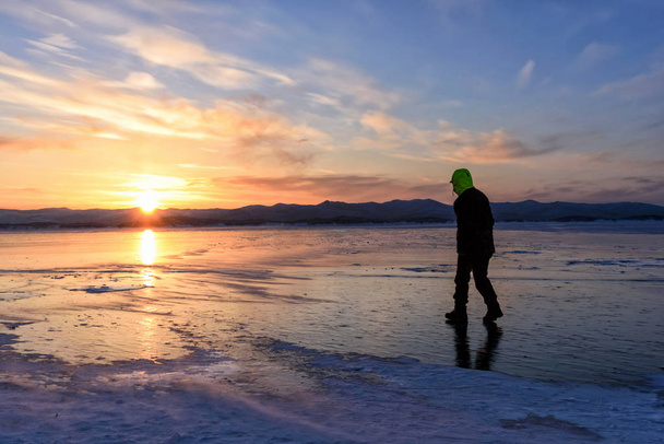 夕焼けのあるバイカル湖の氷の上を歩いている男のシルエット. - 写真・画像
