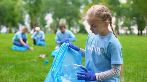Responsible child volunteer collecting trash in garbage bag smiling on camera - Footage, Video