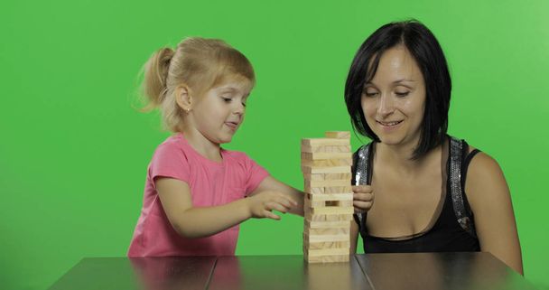 Moeder en dochter spelen de Jenga. Kind trekt houten blokken van de toren - Foto, afbeelding