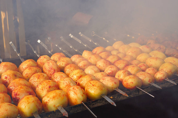 Patatas en la parrilla. Cocinar comida callejera. Los tubérculos de patata se fríen sobre un fuego abierto
. - Foto, Imagen