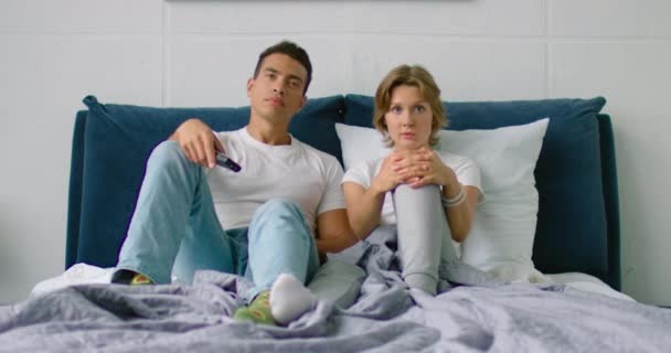 Young mixed couple is watching football, lying in bed, - Imágenes, Vídeo