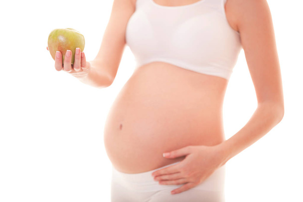Image of pregnant woman touching her big belly and holding apple in the hand isolated on white background. Close up. Beautiful body of pregnant woman. Motherhood, pregnancy. Woman expecting baby - 写真・画像