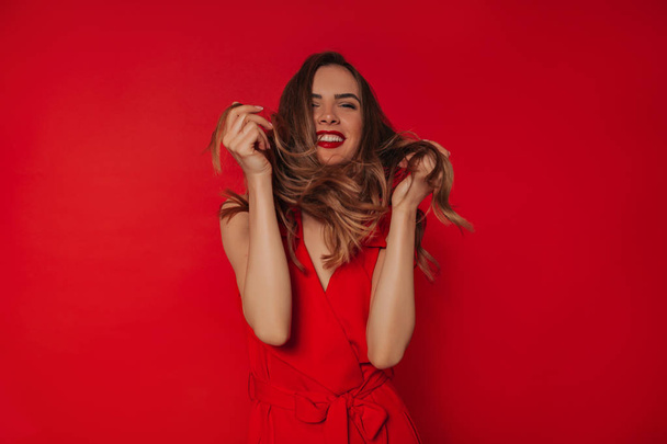 Εμπνευσμένη Ευρωπαϊκή νεαρή γυναίκα έχει τη διασκέδαση στο στούντιο και γελώντας πάνω από το κόκκινο φόντο. Winsome κορίτσι στο χαριτωμένο παίζοντας στο στούντιο - Φωτογραφία, εικόνα