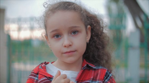 Közelről portré aranyos kaukázusi kislány keresi a kamera, élvezve meleg nyári napon a naplementében. - Felvétel, videó