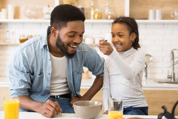 Adorable afro girl feeding her dad cereals - Photo, Image