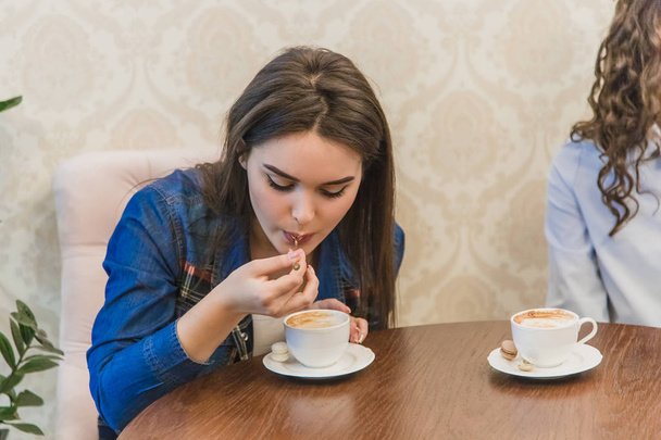 Young pretty girl during a meeting with her girlfriends sitting in a cafe. He is drinking cappuccino and while enjoying it. - 写真・画像