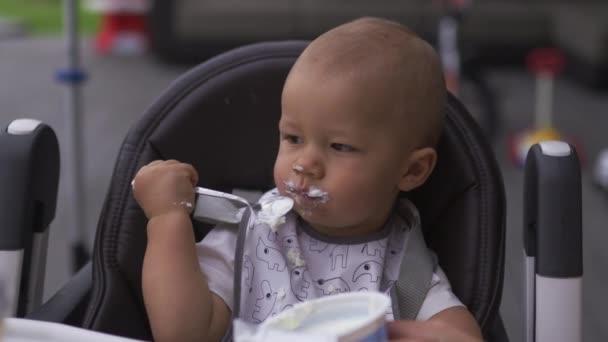 Gesicht aus nächster Nähe lustiger weißer Schnurrbart: junge Mutter füttert ihren kleinen Sohn im Kindersitz - Familie schätzt warme Farbe - Filmmaterial, Video