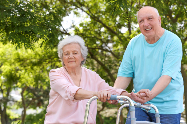 Homem idoso ajudando sua esposa com andar quadro ao ar livre
 - Foto, Imagem