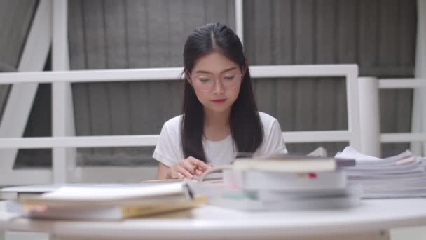 Asijské studentky čtou knihy v knihovně na univerzitě. Mladá vysokoškolská dívka dělá domácí úkoly, čte učebnicovou knížku, pilně studuje znalosti a vzdělání na přednáškové fakultě v pojetí univerzitního kampusu. - Záběry, video
