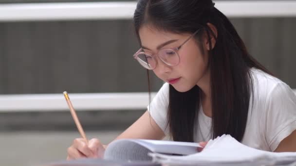 Asijské studentky čtou knihy v knihovně na univerzitě. Mladá vysokoškolská dívka dělá domácí úkoly, čte učebnicovou knížku, pilně studuje znalosti a vzdělání na přednáškové fakultě v pojetí univerzitního kampusu. - Záběry, video