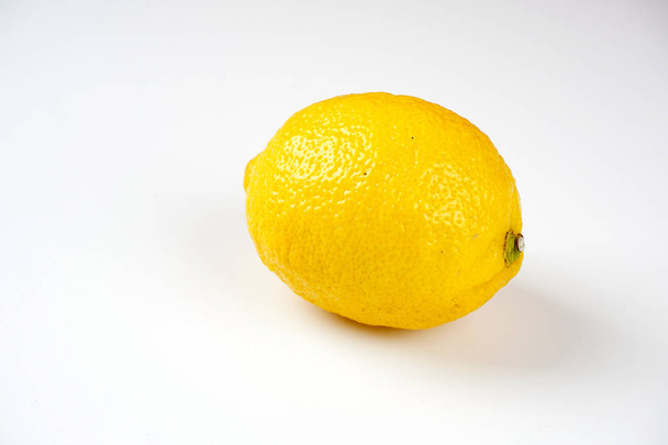 one whole yellow lemon on white table surface  - Фото, изображение