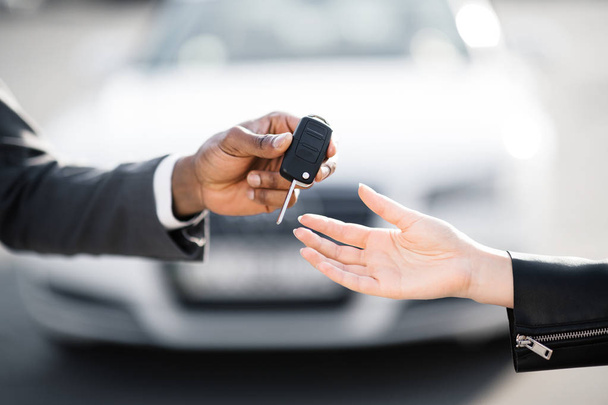 Car salesman handing over keys for new car to young woman - Fotó, kép