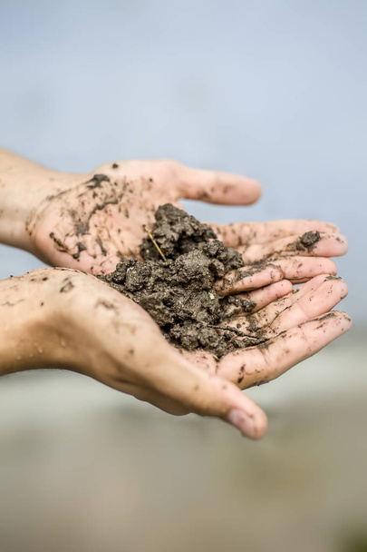Close up of hands of a farmer holding new fresh soil after rain in his hands and showing to the camera. - Photo, Image