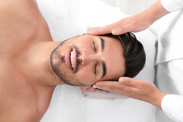 Handsome young man receiving face massage on spa table, top view - Photo, image