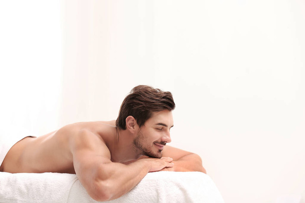 Handsome young man relaxing on massage table against light background, space for text. Spa salon - Foto, imagen