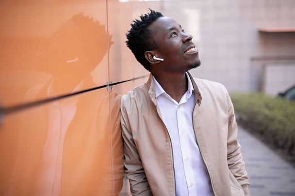 handsome black young man in a jacket and white shirt is listening to music with headphones - Foto, imagen