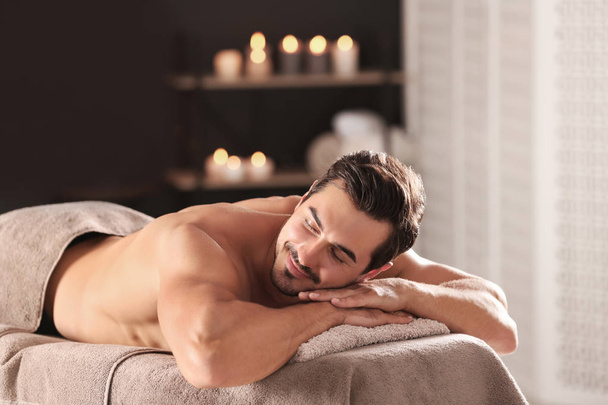 Handsome young man relaxing on massage table in spa salon, space for text - Photo, Image