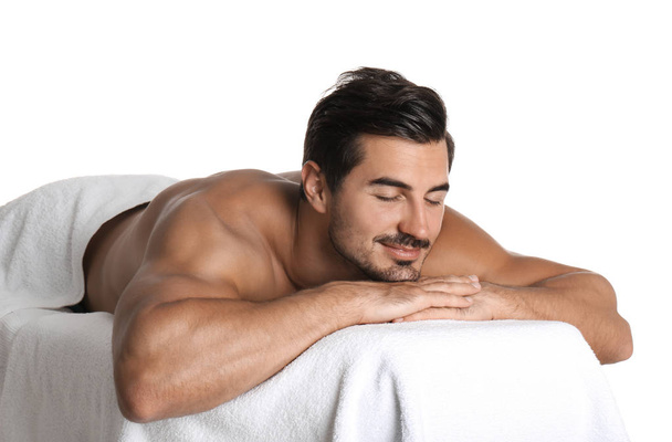 Handsome young man relaxing on massage table against white background. Spa salon - Foto, Imagem