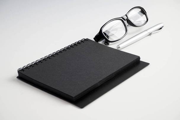 workplace table with eyeglasses, paper textbook and pen on white surface   - Foto, imagen