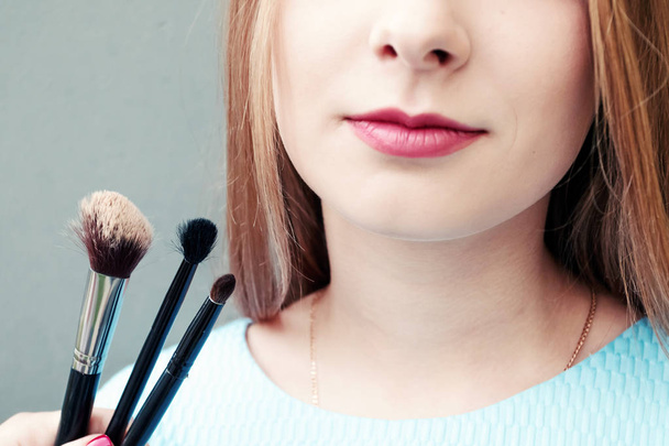 Όμορφη νεαρή κοπέλα με επαγγελματική make-up και πινέλα μακιγιάζ σε γκρι φόντο. Έννοια vzhazhist, μόδα, κοσμετολογία. - Φωτογραφία, εικόνα