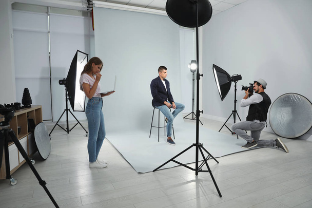 Professional photographer with assistant taking picture of young man in modern studio - Φωτογραφία, εικόνα