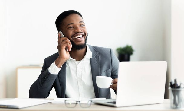 Чорний бізнесмен розмовляє на мобільному телефоні і працює на ноутбуці
 - Фото, зображення